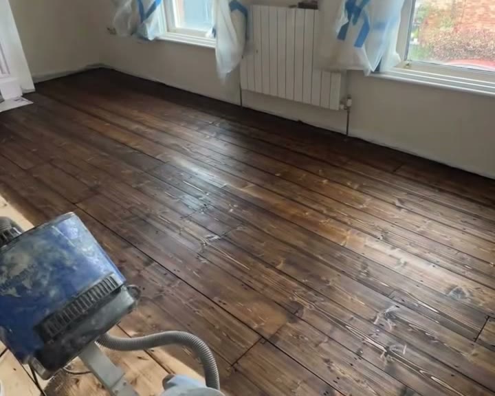 Old floorboards half sanded and stained, with the floor sander in front